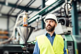 Ein Mann mit einem Helm und einer Weste steht vor Maschinen auf einer Baustelle.